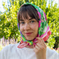 Woman wearing a colorful headscarf outdoors with greenery in the background